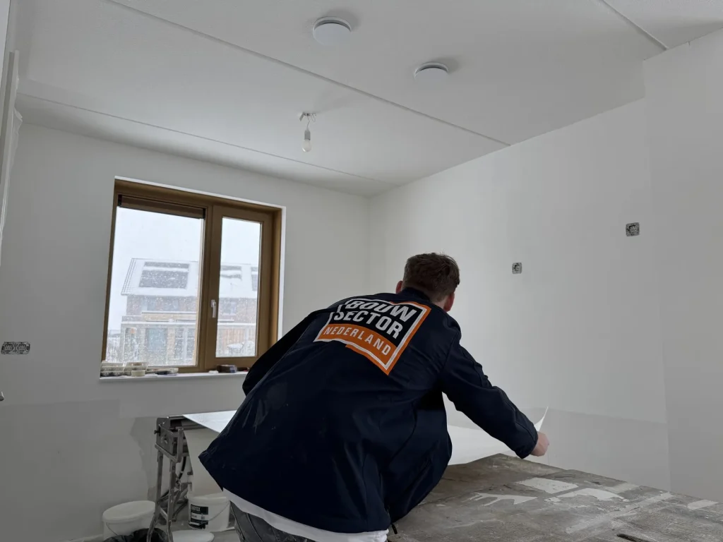 Behanger van Bouwsector Nederland pakt een baan renovlies van de plaktafel in een kale nieuwbouwkamer