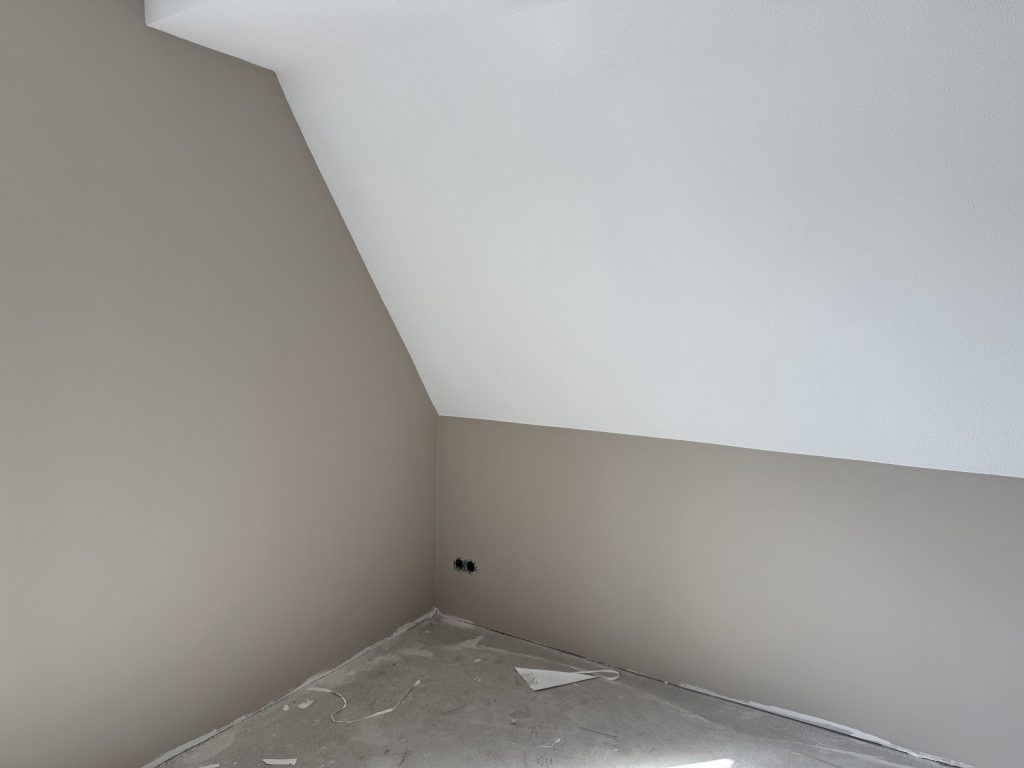 Zolderkamer met een schuine wand en een wit afgewerkt plafond, kort voor de oplevering